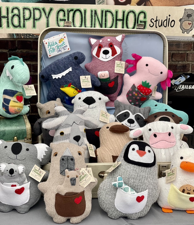 a variety of handmade stuffed animals all made from recycled sweaters. Stuffies are displayed in a vintage suitcase