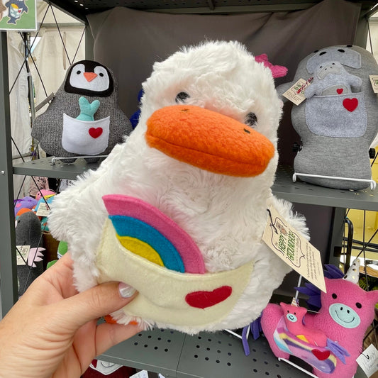 handmade plush duck being held in front of a display with other plushies in an Art show setting