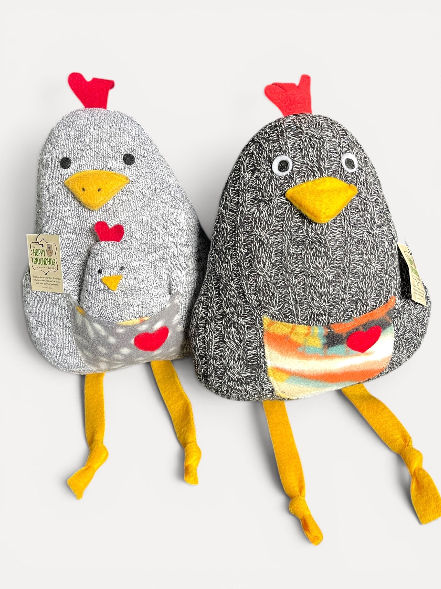 Two plush handmade chickens side by side on a light gray background. One \ is light gray with a speckled texture, red comb, yellow beak and legs, and a small matching pouch.