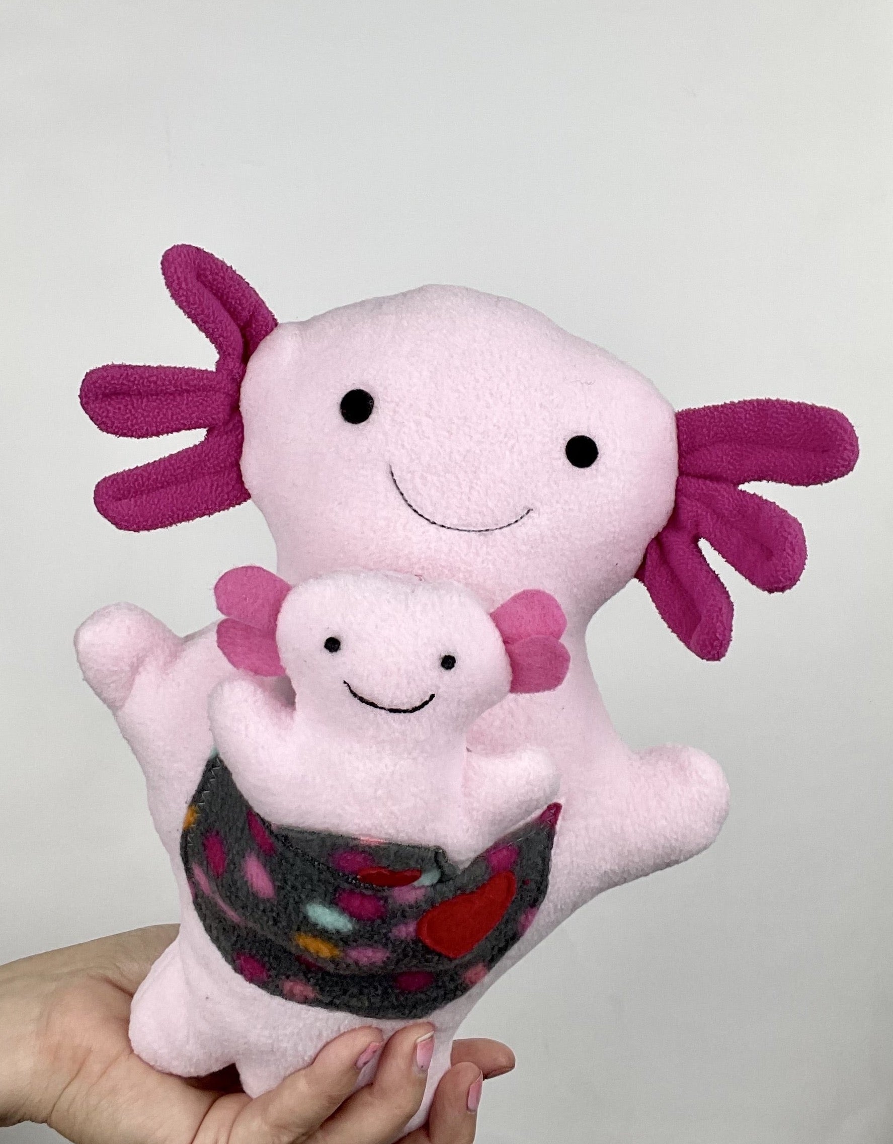 larger pink Axolotl stuffed animal with a baby axolotl stuffed animal in its pocket